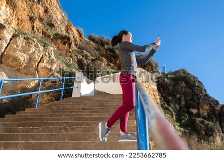 sporty woman standing on steps taking a photo on her phone