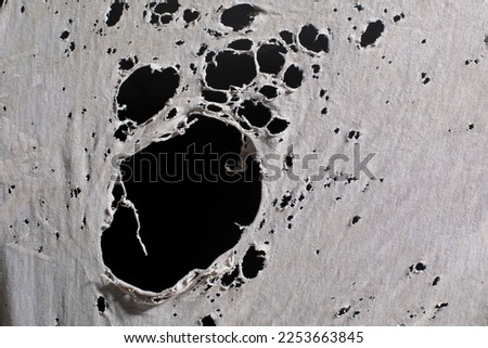 old dirty ragged cloth with holes, grunge damaged cloth on black background, ripped white fabric with many holes Royalty-Free Stock Photo #2253663845