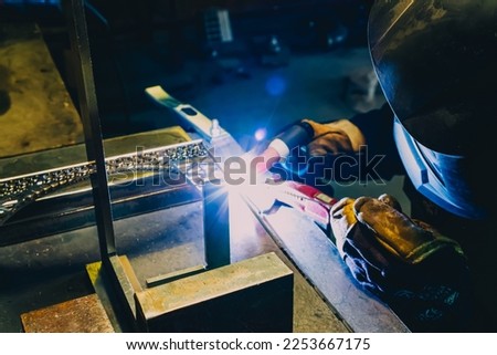 Welder is welding metal eiffel tower. Craft handmade work with electric arc welding machine. Male in face mask for protecting. Industrial steel factory or workshop production.