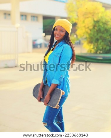 Portrait of happy smiling young african woman with skateboard in the city