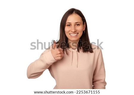 Cute young woman wearing sweatshirt is showing thumb up like gesture over white background.