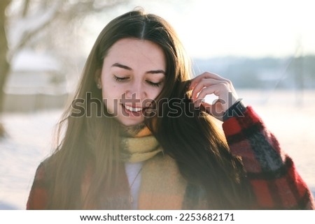 Portrait of a young woman in winter.A girl in a scarf.A woman in a red coat and a plaid scarf.A girl with a beautiful natural smile.Woman posing without makeup.Without retouching. Photo on an old lens Royalty-Free Stock Photo #2253682171
