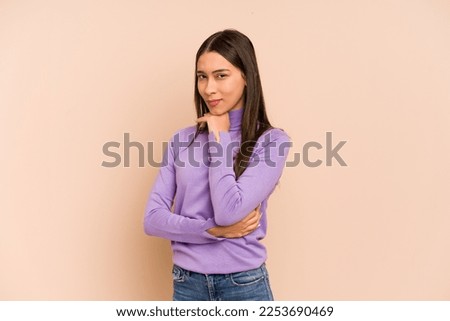Young colombian woman isolated on beige background suspicious, uncertain, examining you. Royalty-Free Stock Photo #2253690469