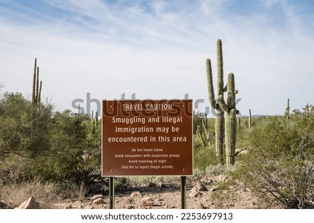 Sign near US - Mexican border wall reading Caution smuggling and illegal immigration in this area - Arizona Royalty-Free Stock Photo #2253697913