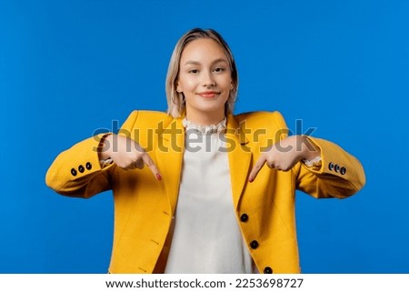 Blonde woman pointing down to advertising area. Blue background. Young woman asking to click to subscribe below. Copy space for your commercial idea, promotional content. High quality photo Royalty-Free Stock Photo #2253698727