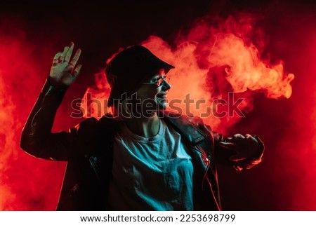 Fashionable woman dancing in red neon light, smoke background. Z generation enigmatic beautiful lady in leather jacket, bucket hat, eyewear. High quality photo
