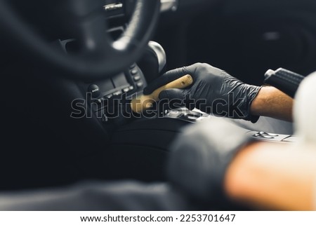 Close-up shot of male hands in black gloves inside car wiping brush over the control panel. Car interior maintenance. Car detailing concept. Horizontal indoor shot . High quality photo