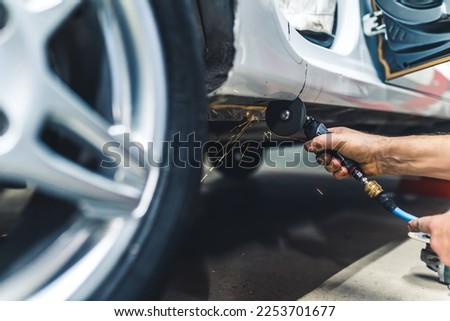 Unrecognisable man using small rotary saw tool to cut out part of body of car. Garage work. Horizontal indoor close-up shot. High quality photo