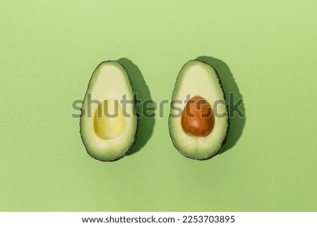 A cut avocado with bone lying on a green isolated background illuminated by hard light close-up. Concept of healthy eating Royalty-Free Stock Photo #2253703895