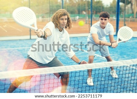 Portrait of focused adult man paddle tennis player during friendly doubles pair match with guy partner at outdoors court