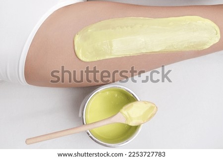 Cropped view from above of green hot wax on woman leg while she lying down on couch. Epilation process in professional beauty salon. Part of photo series.