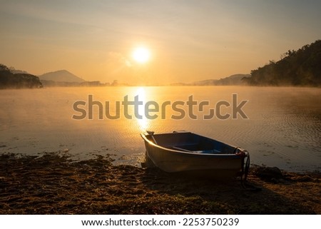 A boat made of fiber was parked on the edge of a beach in the reservoir during the sunrise. at Harirak forest park Huai Nam Man reservoir Loei Thailand 21 Jan 2023