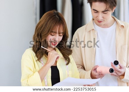 Millennial Asian young professional male female dressmaker designer seamstress colleague with measuring tape standing at workplace using pencil draw sketch dress outline together in tailor studio. Royalty-Free Stock Photo #2253753015
