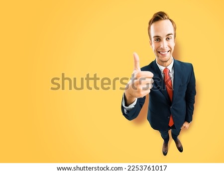 Full body businessman in black suit showing thumb up like, agree hand sign gesture on yellow background. Comic look happy man. Cartoon style character with big head. Funny face. Copy space mockup area