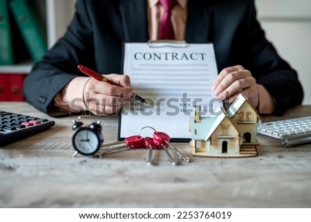 house salesman man in jacket sitting with documents for house sale contract and keys to house model. real estate trading concepts. property insurance