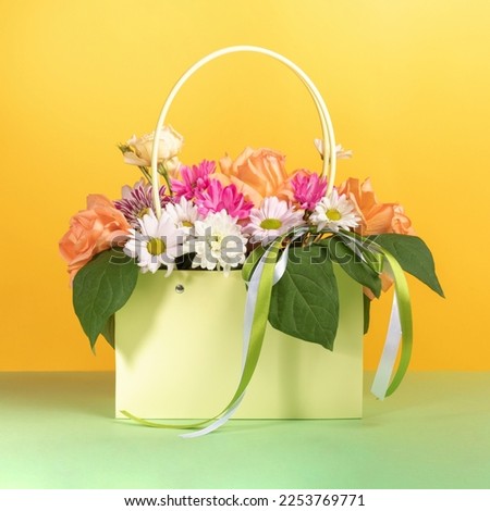Beautiful flowers bouquet in gift light green paper bag with ribbons on yellow-green background. Festive greeting card. Valentine's day, mother's day, wedding, birthday present. Square format.