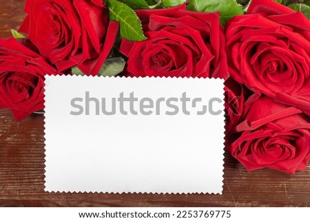 Red roses bouquet and white paper sheet for text on old rustic wooden table close up. Valentine's day, mother's day, wedding, birthday image. Horizontal format. Copy space. Mock up.