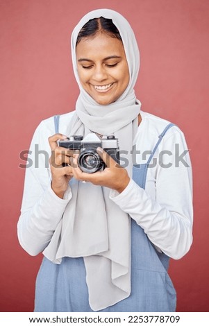 Muslim, hijab and photographer shooting a picture or photo with a retro camera isolated in a studio red background. Islam, Dubai and woman in scarf happy taking creative shots for photography