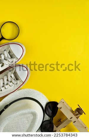 Travel plan, trip and vacation, technology. Top view travel accessories with shoes, straw hat, magnifying glass and wood airplane on yellow background. Copy space. Vertical banner 