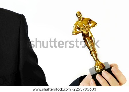 Hand holding Hollywood Golden Oscar Academy award statue on white background. Success and victory concept.