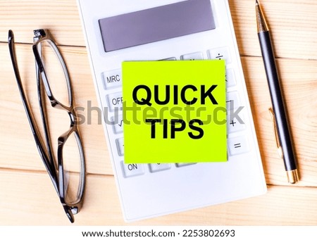 On the desktop there is a green sticker with the text QUICK TIPS, a calculator, glasses and a pen. Top view of the workplace.