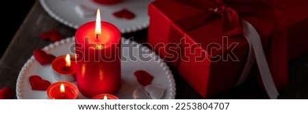 Saint Valentine's Day celebration. Red burning candles, hearts, gift box, postcard on dark wooden background. Happy holiday. Table decor for festive dinner, romantic atmosphere. Banner Royalty-Free Stock Photo #2253804707