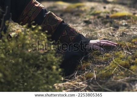 Close up female hand in ethnic clothes touching grass concept photo. Connect with nature. Side view photography with blur background. High quality picture for wallpaper, travel blog, magazine, article