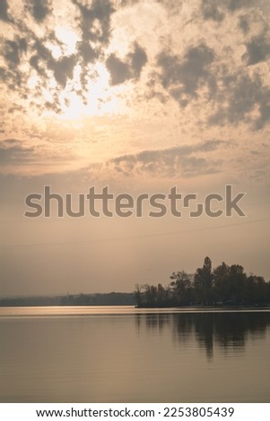 Sunlight through curly clouds above river landscape photo. Beautiful nature scenery photography with blur background. Idyllic scene. High quality picture for wallpaper, travel blog, magazine, article