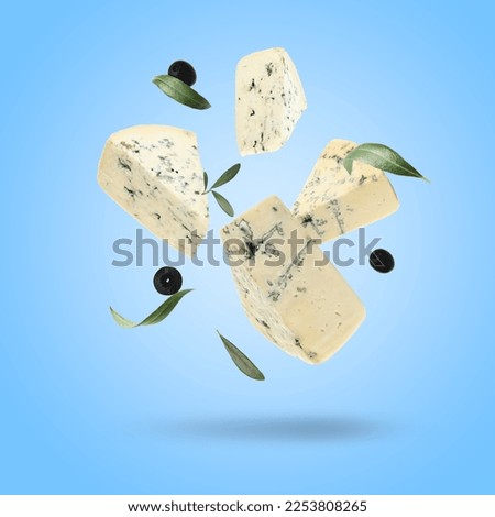 Pieces of delicious cheese, olives and leaves falling on light blue background Royalty-Free Stock Photo #2253808265
