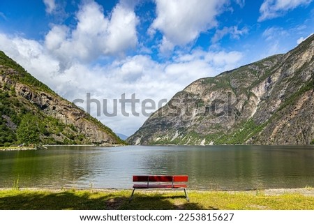 Red wooden bench on the bank of the huge and picturesque Sognefjord. Warm sunny day in July. Northern Europe. Summer trip to Norway. 
