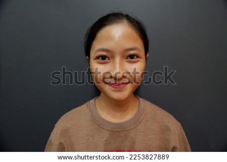 Portrait of Indonesian Young Girl with no make up standing on a grey background in studio. Royalty-Free Stock Photo #2253827889