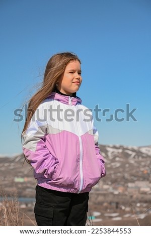 A teenage girl walks through the mountains. Happy young girl in a jacket in the wind. A walk in the fresh air.