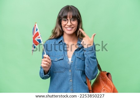 Young caucasian woman holding an United Kingdom flag over isolated background giving a thumbs up gesture