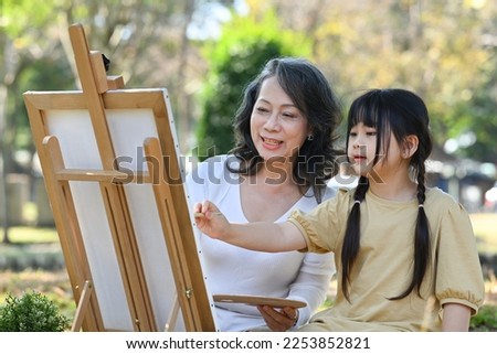 Happy middle aged grandma painting picture with lovely little grandchild, enjoying leisure weekend activity together outdoor