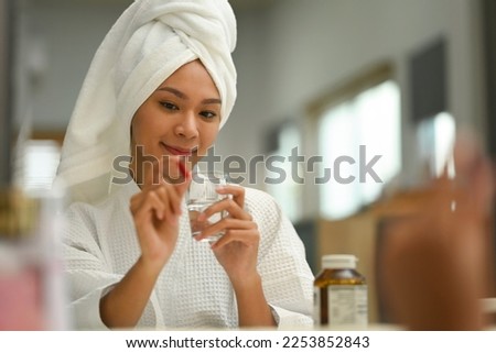 Smiling millennial lady holding glass of water taking dietary supplement. Beauty Supplement concept