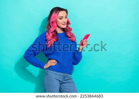 Photo of shiny positive girl with curly hairdo dressed blue sweater look at phone read sms isolated on vibrant teal color background