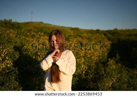 A teenage girl walks through the mountains, across the field. A happy young girl with long hair, standing in the wind. A walk in the fresh air.