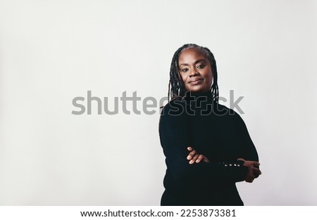Mature woman with dreadlocks looking at the camera in a studio. Elegant middle-aged woman standing against a grey background with her arms crossed.