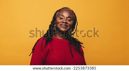 Portrait of a mature woman with dreadlocks smiling at the camera while standing against a yellow background. Happy black woman embracing her natural hair.