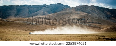 The car drives quickly through the mud with clouds of dust from under the wheels, against the backdrop of the mountains. Rally Dakar. Off-road vehicle rides off-road in the desert. Royalty-Free Stock Photo #2253874021