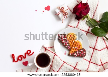 Romantic breakfast, fresh baked homemade heart shaped Belgian waffles with chocolate topping, cup of tea or coffee and red rose on white table. Valentine's Day surprise concept. Minimalistic flat lay