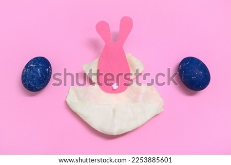 Easter Bunny in a cabbage leaf. Laying out the painted eggs. Concept. Pink background