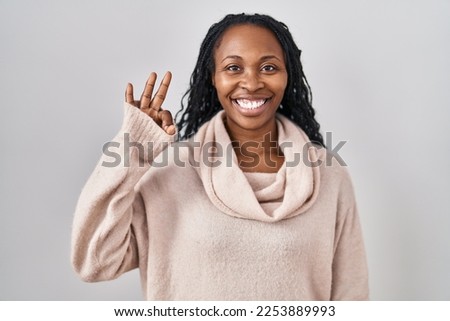 African woman standing over white background smiling positive doing ok sign with hand and fingers. successful expression. 