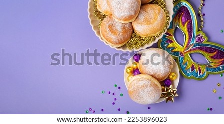 Mardi Gras King Cake doughnuts or donuts, masquerade festival carnival mask, gold beads and golden, green confetti on purple background. Holiday party invitation, greeting card concept. Royalty-Free Stock Photo #2253896023