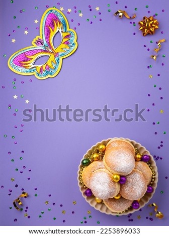 Mardi Gras King Cake doughnuts or donuts, masquerade festival carnival mask, gold beads and golden, green confetti on purple background. Holiday party invitation, greeting card concept.