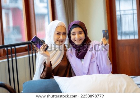 Two Muslim women wearing a hijab using a smartphone, shopping online with a credit card. muslim women online shopping.