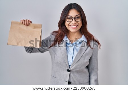 Hispanic young woman holding take away bag looking positive and happy standing and smiling with a confident smile showing teeth 