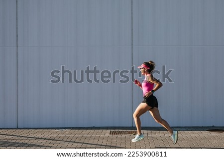 Sporty woman running in the street. Pink clothes and cap.