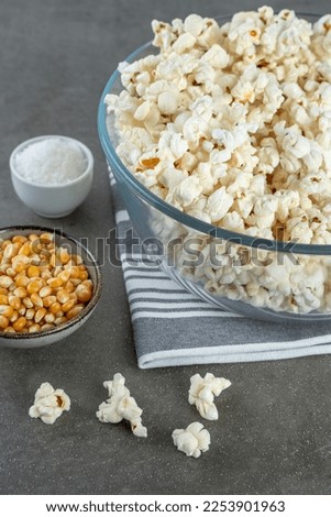 popcorn in a bowl, salt and popcorn kernels on a gray striped napkin on a gray concrete background, close-up and selected focus.