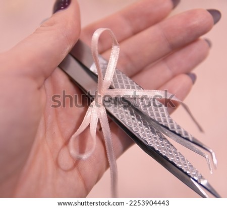 Close up of flat and curved metal tweezers for eyelash extensions in hand on pink background with bow . High quality photo